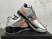 Pair of silver Nike KD basketball shoes with orange accents, midfoot straps, and translucent-looking outsoles.