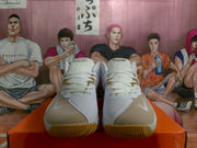 Front view showing the white and yellow-gold Nike basketball sneakers with textured toe panels and gum-colored traction outsoles.