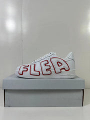 Side view of a white low-top sneaker with oversized red-outlined AIR lettering, displayed on a gray shoebox.