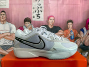 Side profile of one Nike basketball sneaker showing the black Swoosh, gray paneling, beige forefoot, and visible Zoom marking on the midsole.