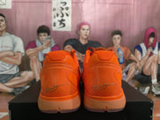Rear view of the orange sneakers showing the structured heel, signature-style heel graphic, and translucent-looking outsole.