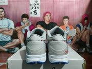 Rear view of gray and white Nike basketball sneakers with blue outsole accents and red heel detailing.