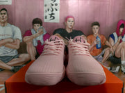 Front view of pink Nike sneakers with matching laces on an orange shoe box.