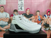 Side view of a white, grey and silver high-top Under Armour basketball sneaker on a black box.