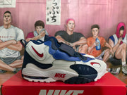 Side view of a Nike sneaker showing the layered color-blocked upper, front strap, AIR branding, and chunky outsole.