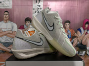 Gray-green Nike basketball sneakers displayed on a shoebox, showing black Swoosh branding, perforated panels, and pale green accents.