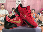 Angled view showing the red upper, gold swoosh-style side branding, black outsole sections, and heel graphics.