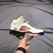 Side view of a white high-top sneaker showing the patterned side panel, number 23 detail, black midsole, and orange accents.