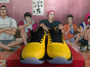 Front view of yellow and black sneakers with black laces, perforated toe areas, and black-and-gold tongue details.