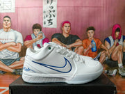 Side view of a white basketball shoe with blue side detailing and a signature-style heel graphic.