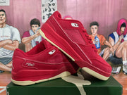 Angled view of a pair of red sneakers showing the side mesh panels, script detailing, Jumpman tongue emblem, and cream-colored outsole sections.