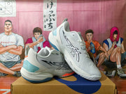 Two white basketball shoes arranged at an angle, showing black side detailing, pale blue heel panels, and coral accents.