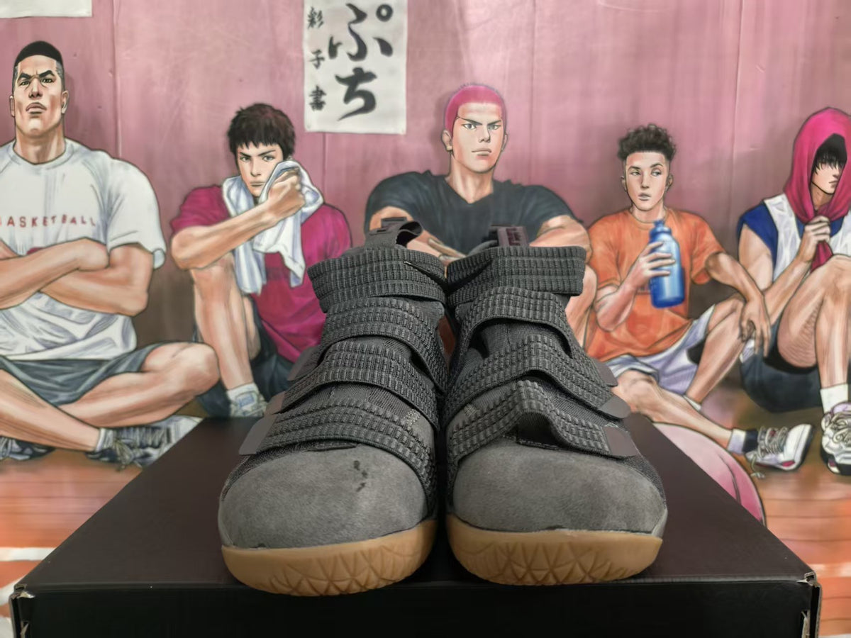 Front view of cool gray Nike basketball sneakers with multiple straps and gum-colored outsoles on a shoebox.
