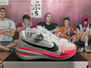 Side view of a white Nike basketball shoe with a black Swoosh, pink and orange accents, and a speckled sole.