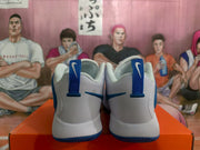 Rear view of white and blue Nike basketball sneakers showing blue heel pull tabs, blue outsole edges, and padded collars.