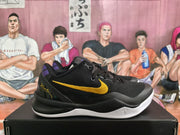 Side view of a black Nike sneaker showing the yellow Swoosh, purple heel detail, black laces, and white outsole.
