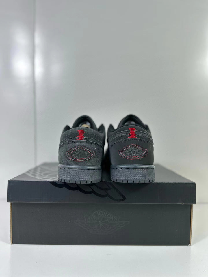 Rear view of dark grey and black low-top sneakers with red heel details on a shoebox