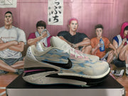Side profile of the sneaker pair showing the blue patterned upper, black Swoosh, layered midsole, pink accent, and black outsole.