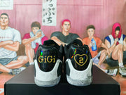 Rear view of black and white basketball sneakers showing gold “GiGi” and shield-shaped “2” heel graphics.