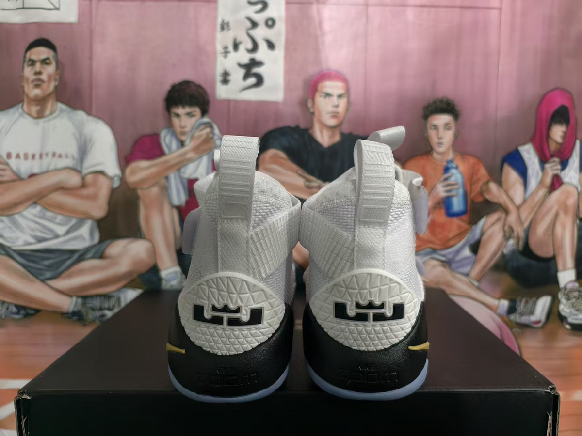 Rear view of white and black high-top basketball sneakers with gold accents, textured collars, and heel details.