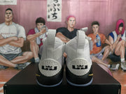 Rear view of white and black high-top basketball sneakers with gold accents, textured collars, and heel details.