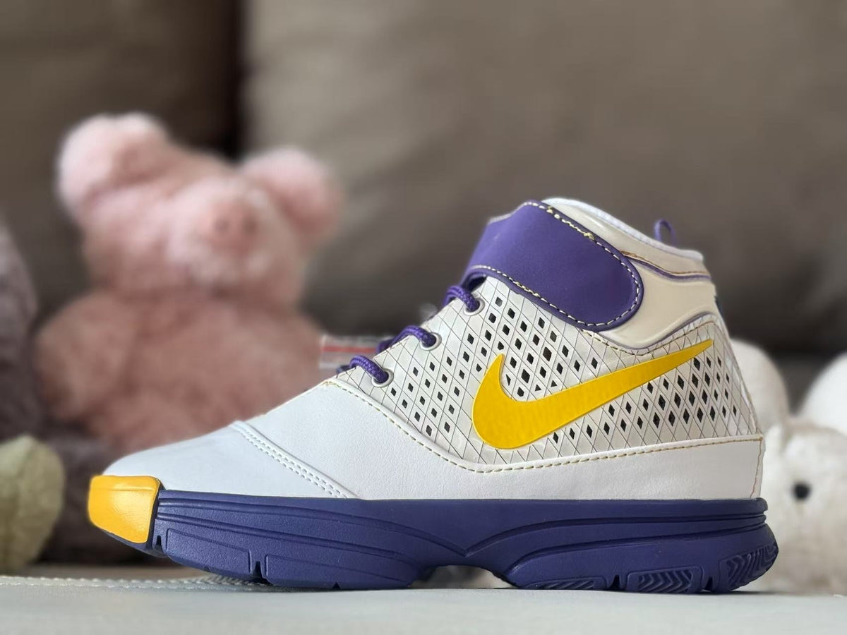 Side profile of a white high-top kids' basketball sneaker with purple ankle overlay, yellow Swoosh, patterned side panel, and dark purple outsole.