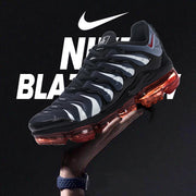 Nike Air VaporMax Plus sneaker shown at an angle, with a black and gray patterned upper and red sole.