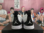 Rear view of white and black high-top sneakers showing glossy black heel panels, white midsoles, black outsoles, and visible Jumpman-style logos.