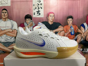 Side view of a white Nike basketball sneaker with blue speckled branding, an orange midsole accent, and a gum-colored outsole.