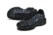 Angled view of black Nike Air Max Plus sneakers with blue outlined lettering and light blue Swoosh details.