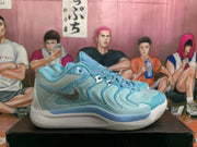 Side profile of an ice blue and grey Nike basketball sneaker with layered panels, perforations, and a blue outsole accent.