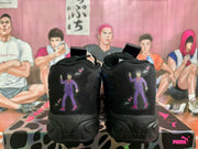 Rear view of black Puma sneakers with purple character artwork on the heels, placed on a Puma shoebox.
