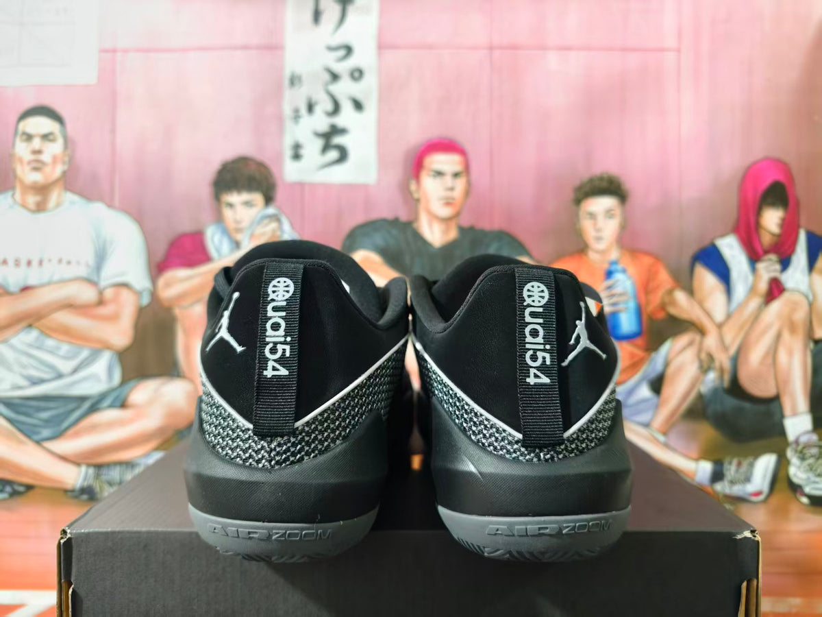 Rear view of black and grey Jordan basketball sneakers displayed on a black shoebox, with Jumpman logos and AIR ZOOM branding visible.