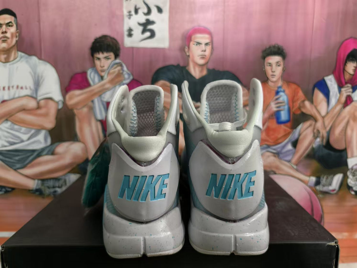 Rear view of white and light blue Nike high-top basketball sneakers with blue heel branding, displayed on a black shoebox.