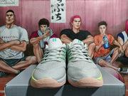 Front view of light gray-white Nike basketball shoes with teal and lime accents and gum-toned outsoles.