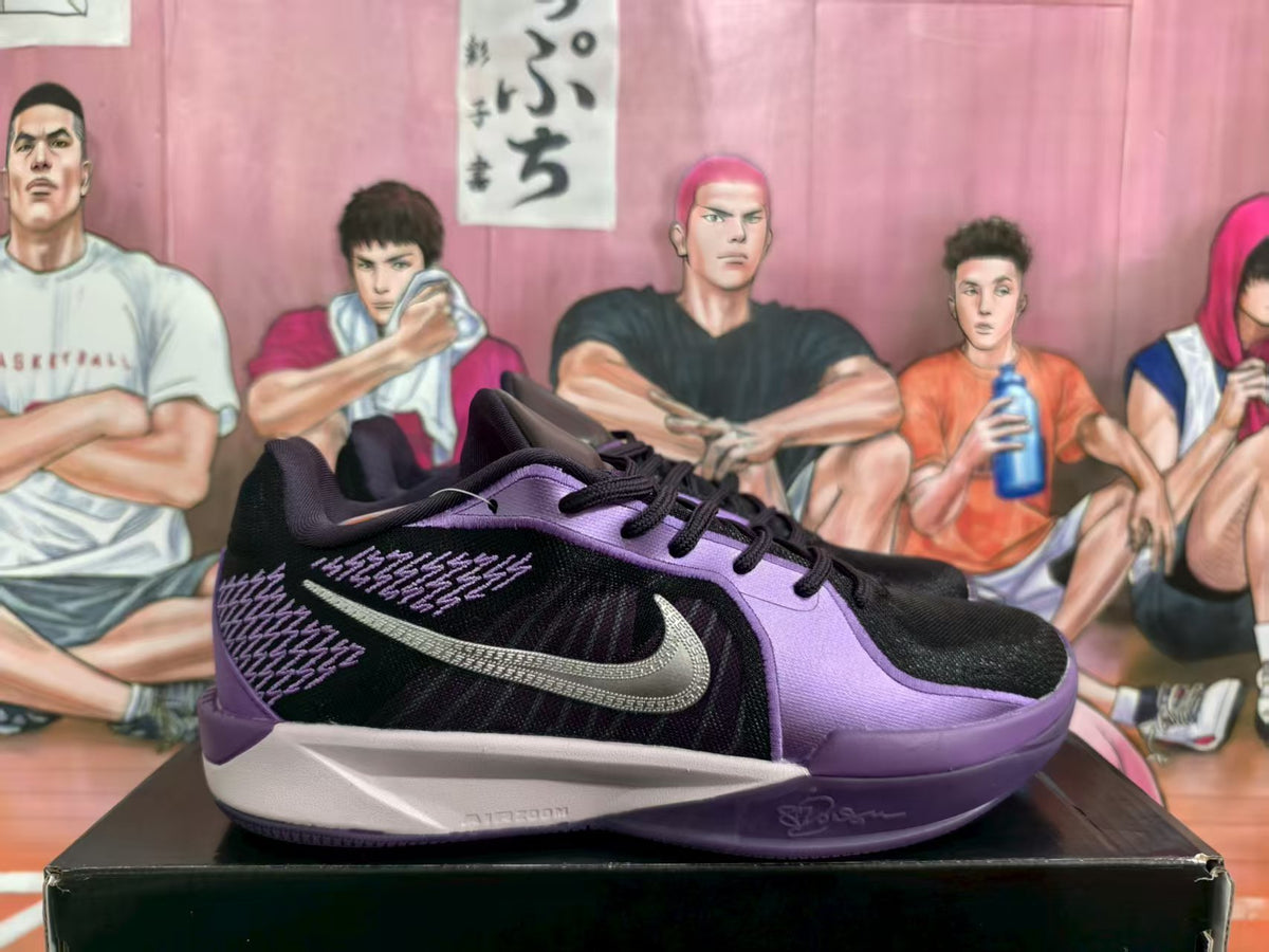 Side view of a black and purple Nike basketball sneaker on a box.