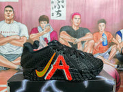 Side view of black Nike sneakers with an orange swoosh, large red side graphic, textured upper, and patterned outsole.