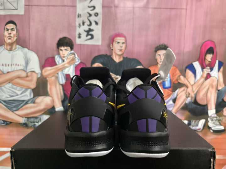 Rear view of black Nike basketball shoes with purple heel accents and white outsoles on a box.