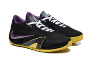 Angled view of a pair of black basketball shoes with white laces, purple accents, and gold-colored outsoles.