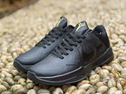 Front three-quarter view of black low-top sneakers with perforated toe boxes, black laces and gold tongue logos.