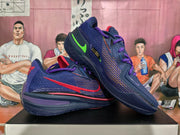 Angled view of two purple Nike basketball sneakers showing the textured sides, red and green branding accents, and patterned outsoles.