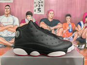 Side profile of a black high-top basketball sneaker showing perforated overlays, a circular heel detail, white midsole sections, and a red outsole edge.