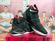 Angled view of black Nike LeBron basketball shoes with red details and white soles.