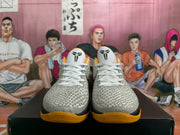 Front view of the basketball sneakers showing white laces, textured light uppers, black tongue logos, and gold-orange outsoles.