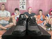 Pair of black and gray basketball sneakers shown from the front with patterned uppers, black laces, white tongue emblems, and a basketball-themed backdrop.