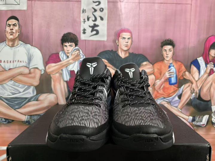 Pair of black and gray basketball sneakers shown from the front with patterned uppers, black laces, white tongue emblems, and a basketball-themed backdrop.