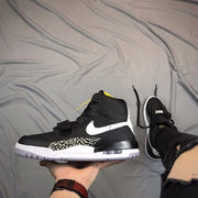 Side view of a black and white high-top sneaker with a forefoot strap, white Swoosh, elephant-print panel, and visible heel cushioning window.
