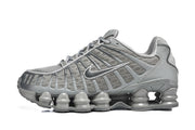 Side view of a grey Nike Shox TL sneaker showing its mesh upper, layered panels, side logo and segmented sole.