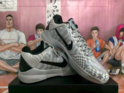 Angled view of Nike basketball sneakers showing the black Swoosh, grey laces, geometric patterned upper and light-coloured sole.