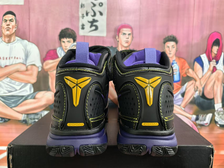 Rear view of black high-top basketball sneakers with purple collars and midsoles, yellow stitching, and yellow heel emblems.